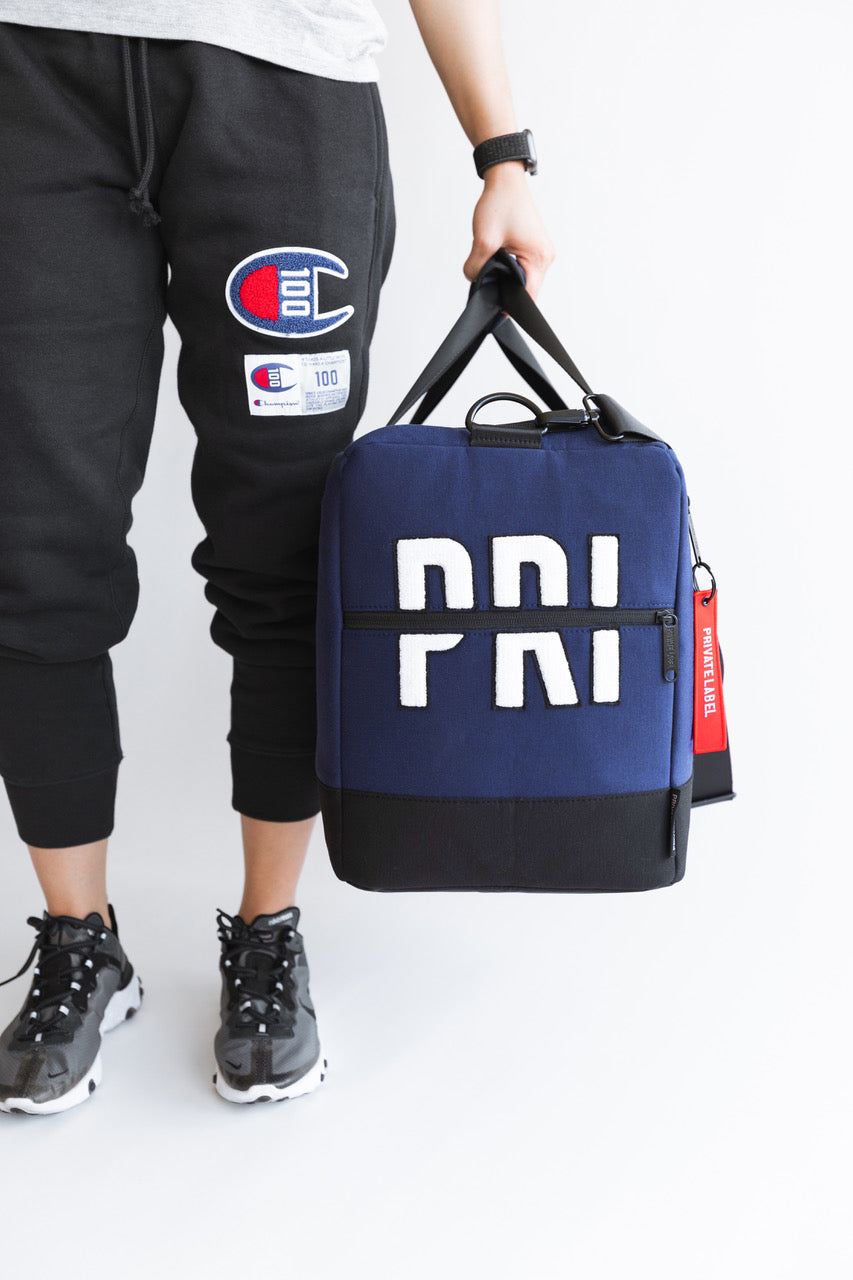 Champion x Private label navy duffle bag with a model wearing a matching champion fleece pants