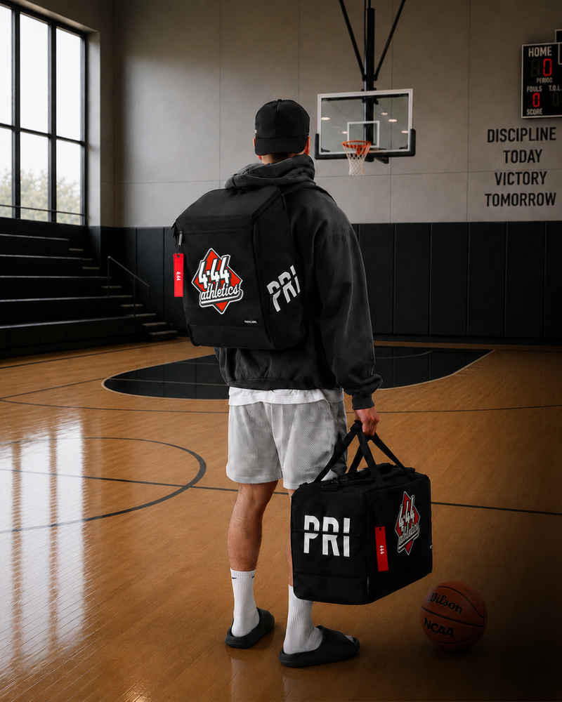 Person holding a black duffel bag with 'PRI' branding on a basketball court.