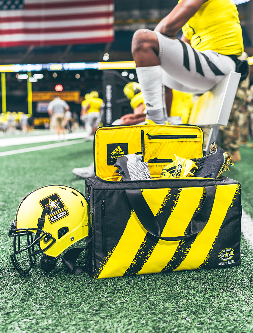 Black bag with 3 yellow stipes in a football arena with a football player sitting behind the bag