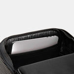 Close-up of an open black backpack or laptop bag showing a padded interior compartment with a silver laptop inside, on a light gray background.