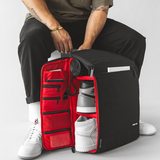 model opening side panel of a black backpack to show how items can be neatly stored inside the bag