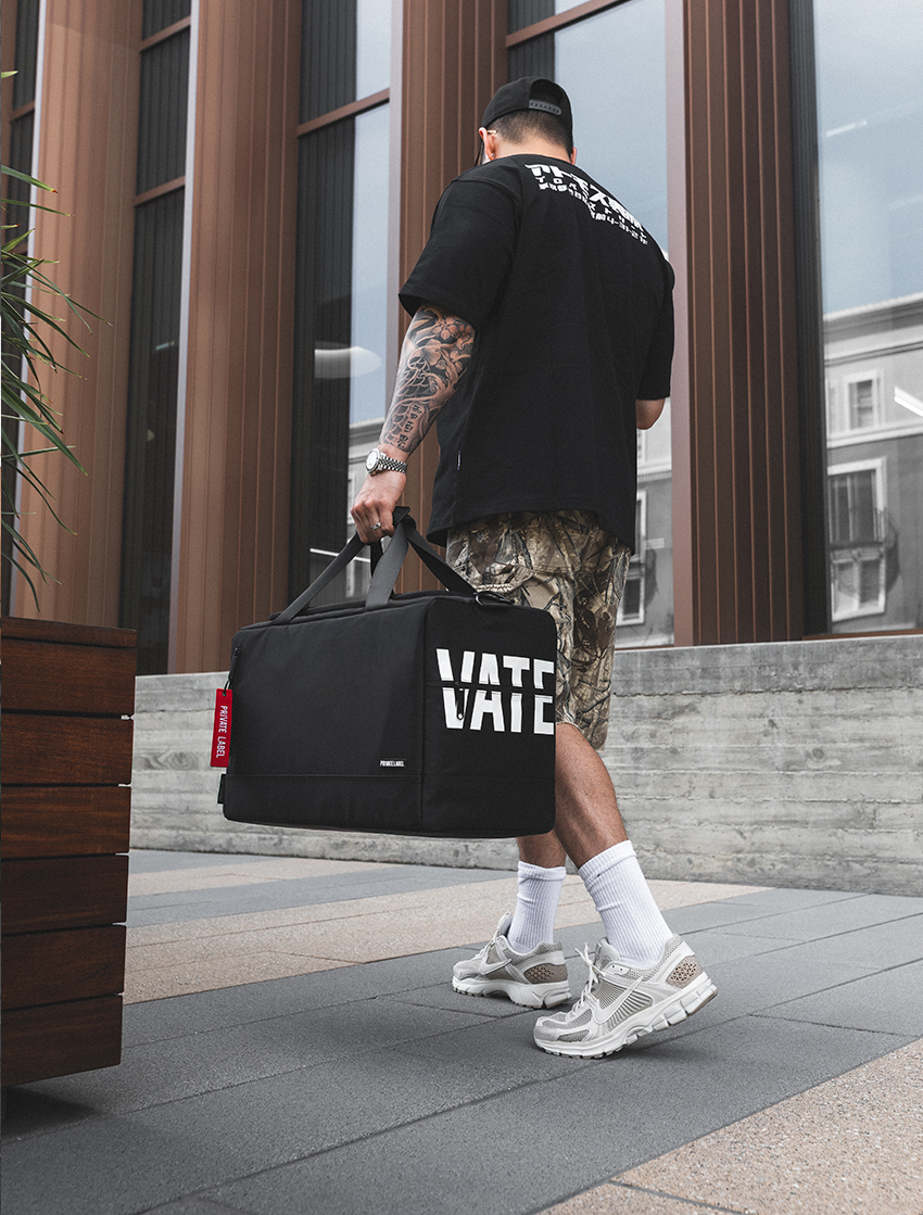 Person walking with a black duffel bag featuring 'Vans' branding on a city street.
