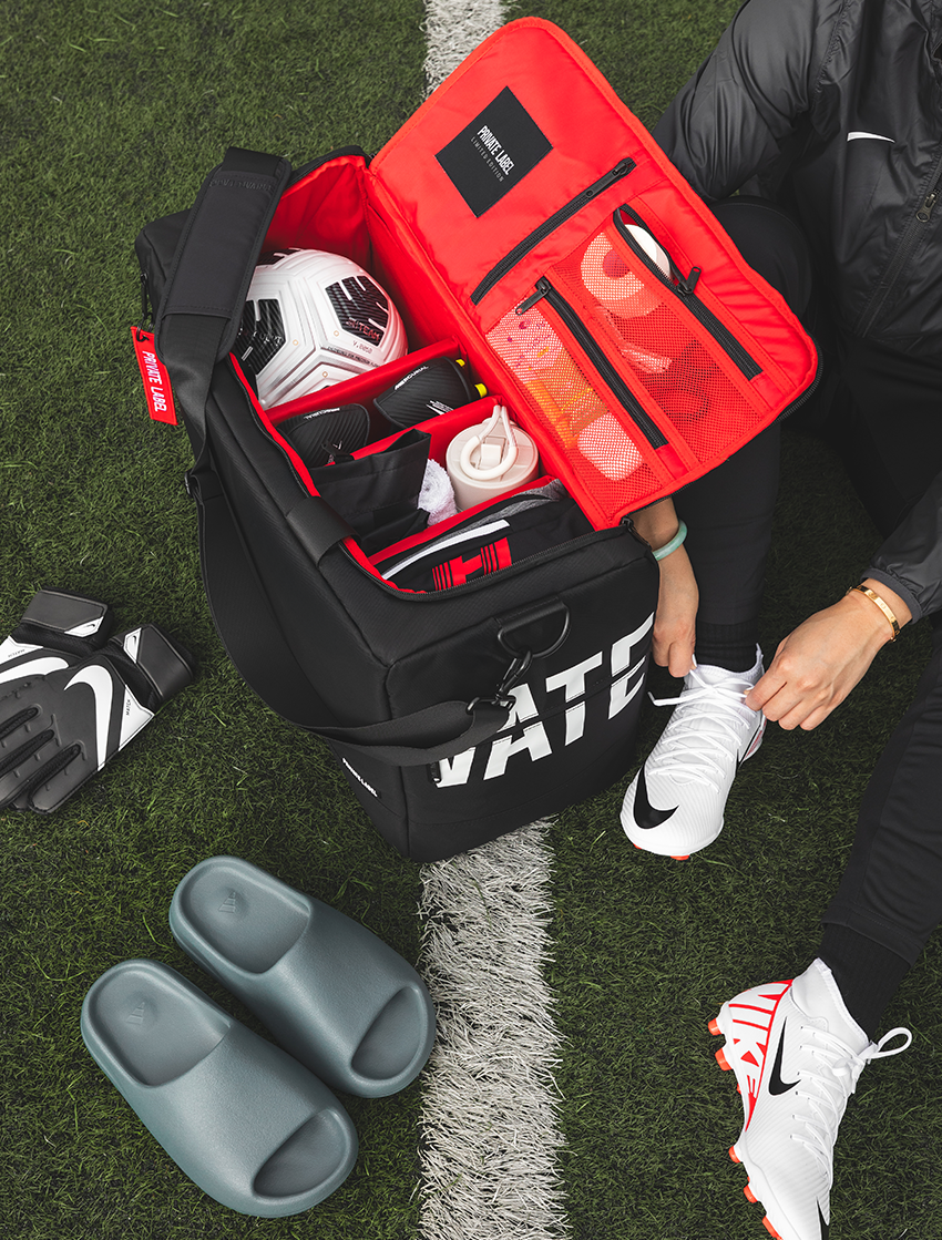 Soccer player on the field with a black duffle with red interior packed with soccer gear