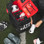 Soccer player on the field with a black duffle with red interior packed with soccer gear