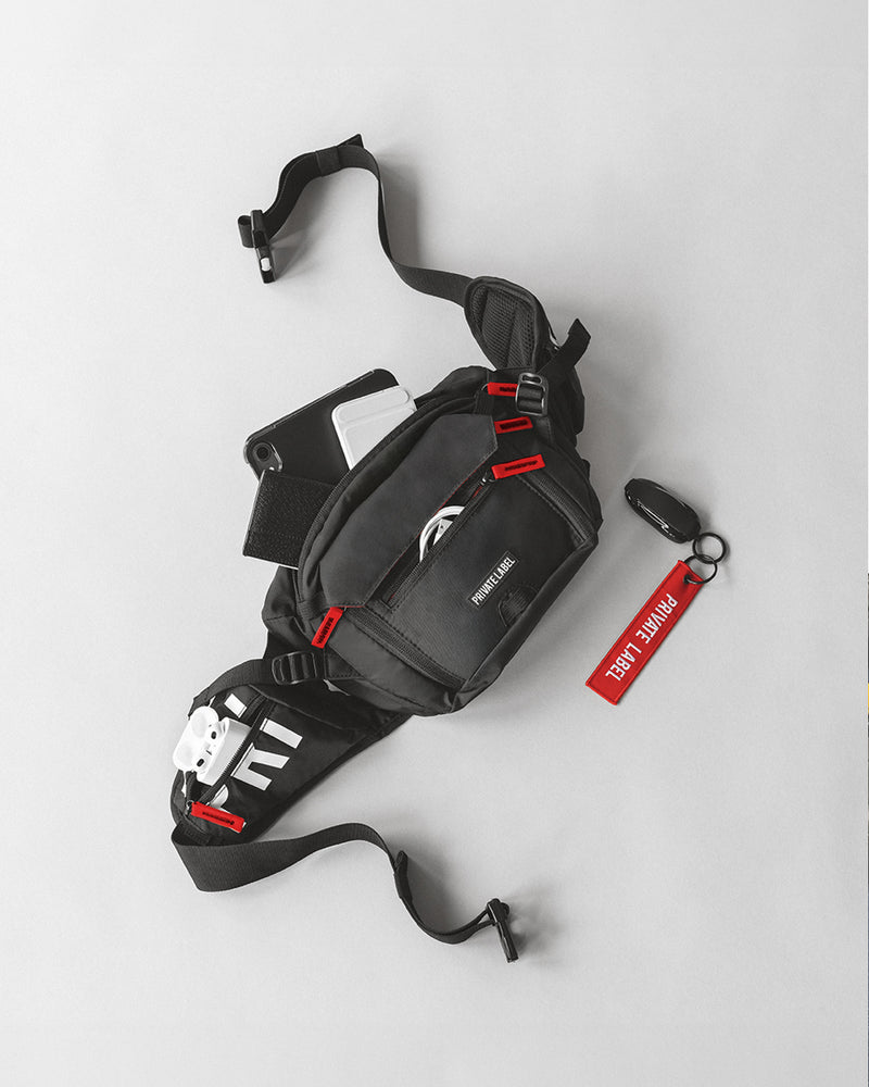 stand alone image of a black bag with red accents showing tech gear, wires, and wallet packed inside the bag along with a car key attached to a red key chain