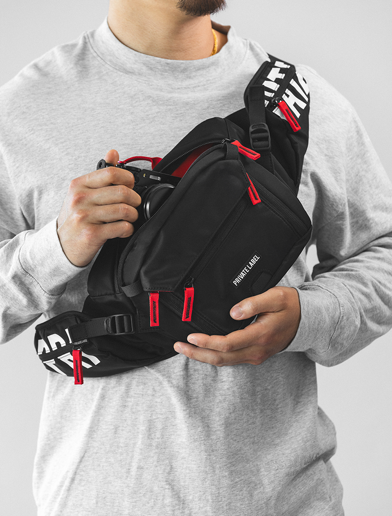 model wearing a black sling bag with red accents pulling out a camera from the bag