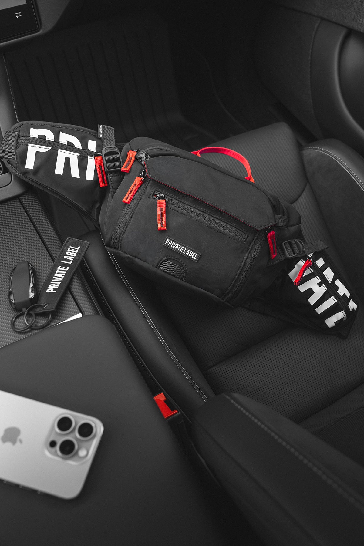 Black and red PRIVATE LABEL sling bag with its front pocket zipped closed on a car seat.