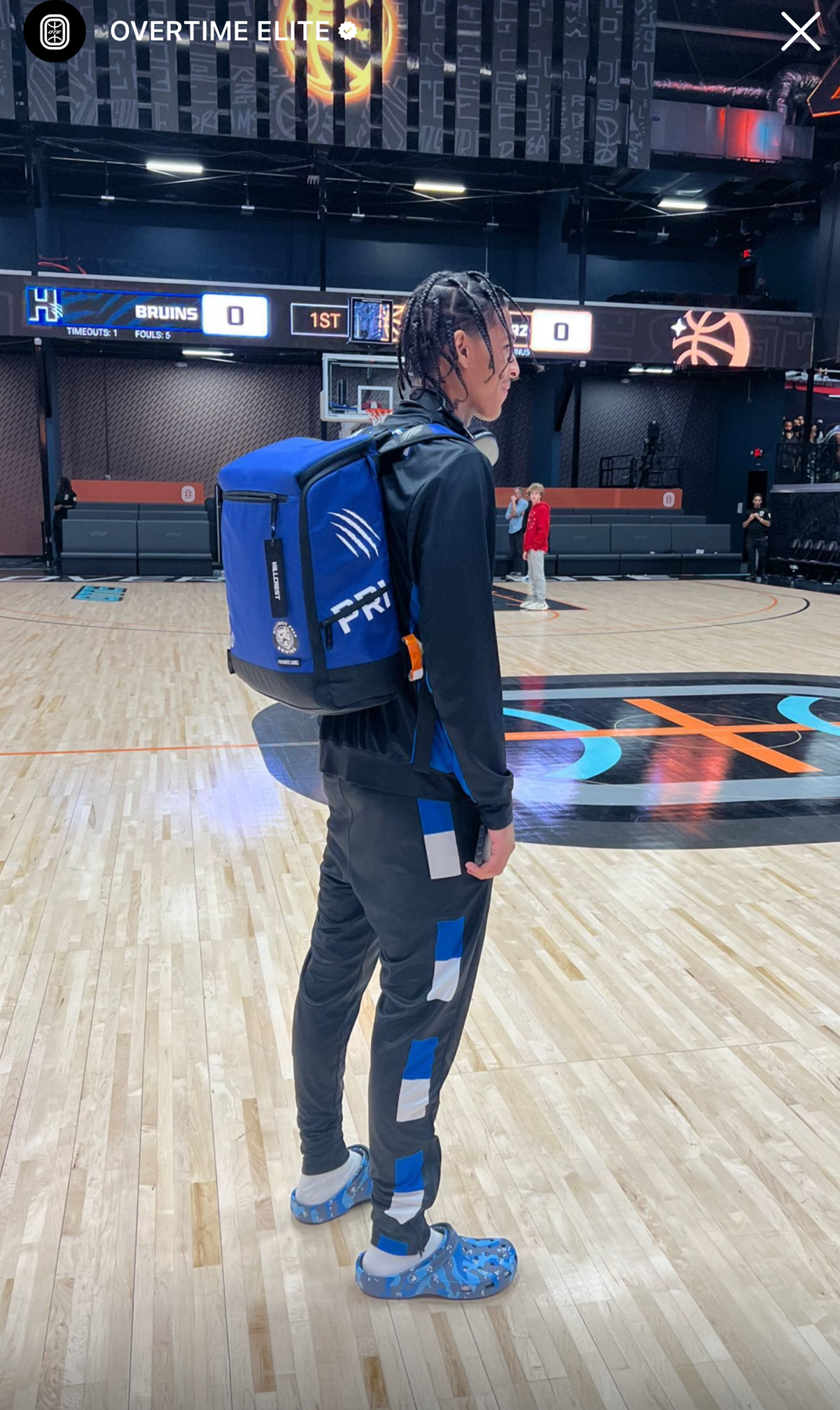 Person wearing a blue backpack with a logo on a basketball court