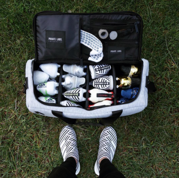 Open private label duffle on grass with various shoes and sports equipment