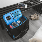 Black bag with light blue interior with shoes and clothes packed inside, sitting in a living room