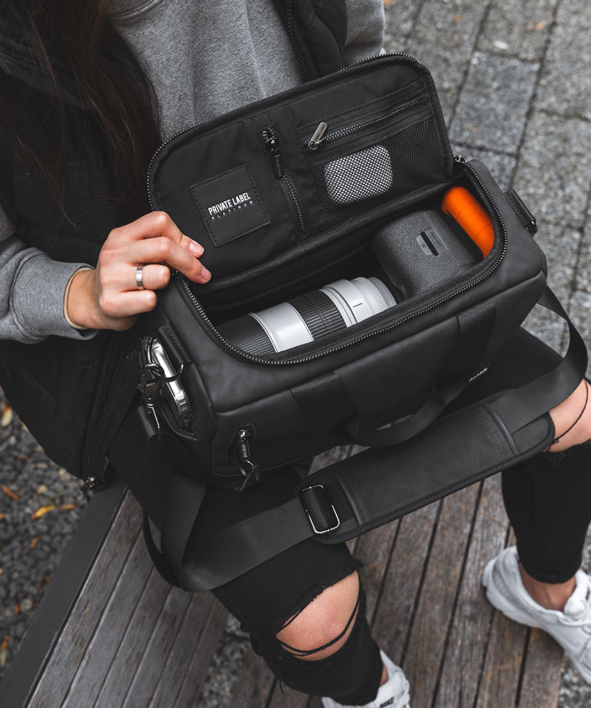 model holding a black duffle bag opened & showing a camera inside along with camera accessories