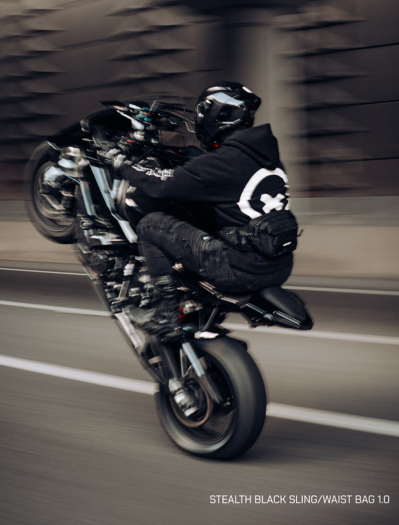 Person wearing a black waist bag riding a motorcycle with a blurred background