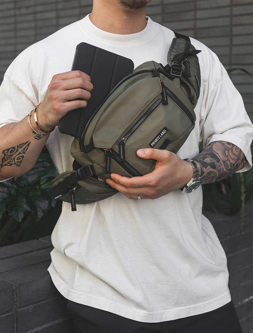 Model wearing green sling bag on chest pulling out tablet from bag