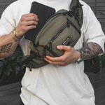 Model wearing green sling bag on chest pulling out tablet from bag
