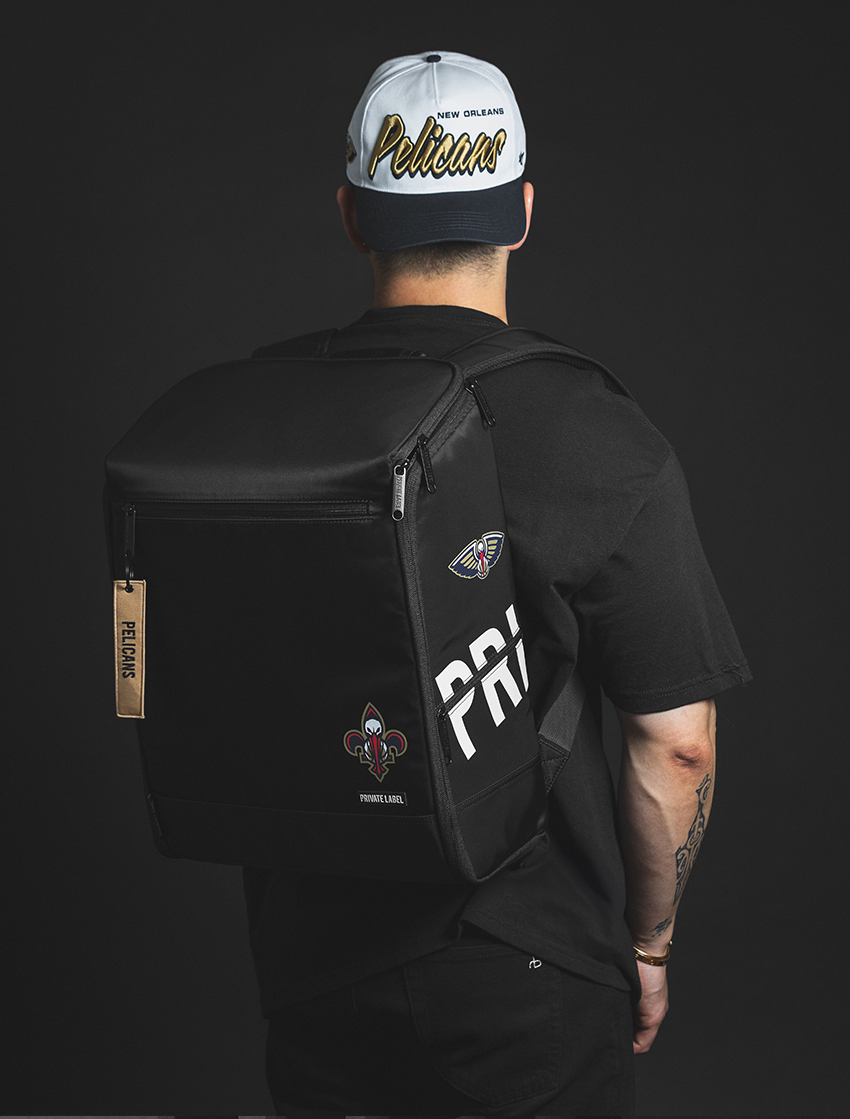 Person wearing a black backpack with branding, a black t-shirt, and a white cap with text on a dark background