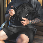Person sitting on a bench holding a black bag with visible branding.