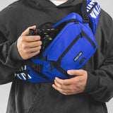 Model wearing blue sling bag on front chest pulling out a camera