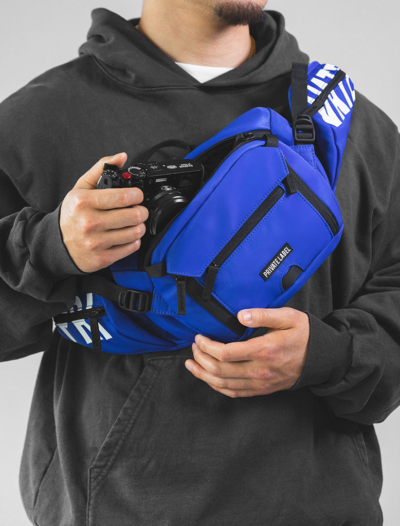 Model wearing blue sling bag on front chest pulling out a camera