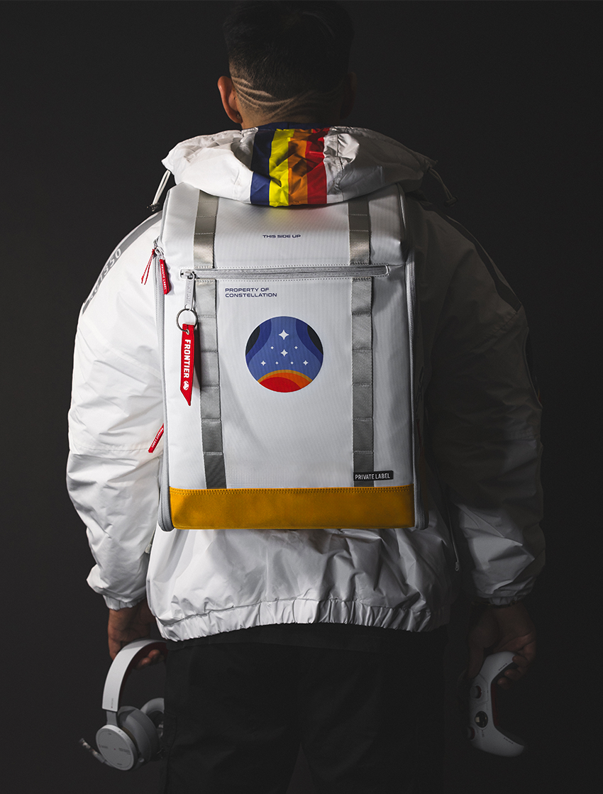model wearing a white jacket and a starfield branded white backpack while holding a controller and headphones