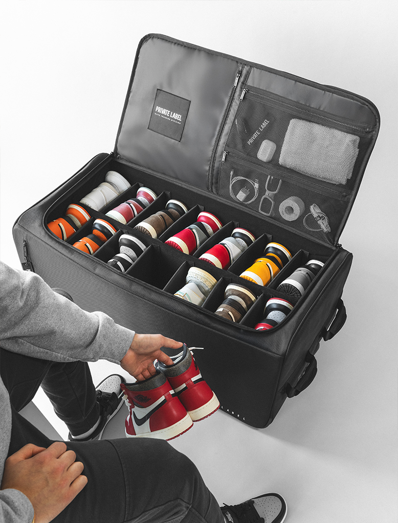 Black bag with shoes organized with compartments filled with various shoes, held by a person sitting on the floor.