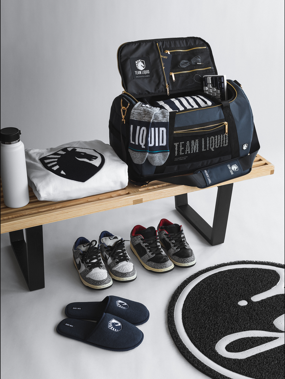 Team Liquid branded bags & accessories placed on a bench with shoes & travel gear