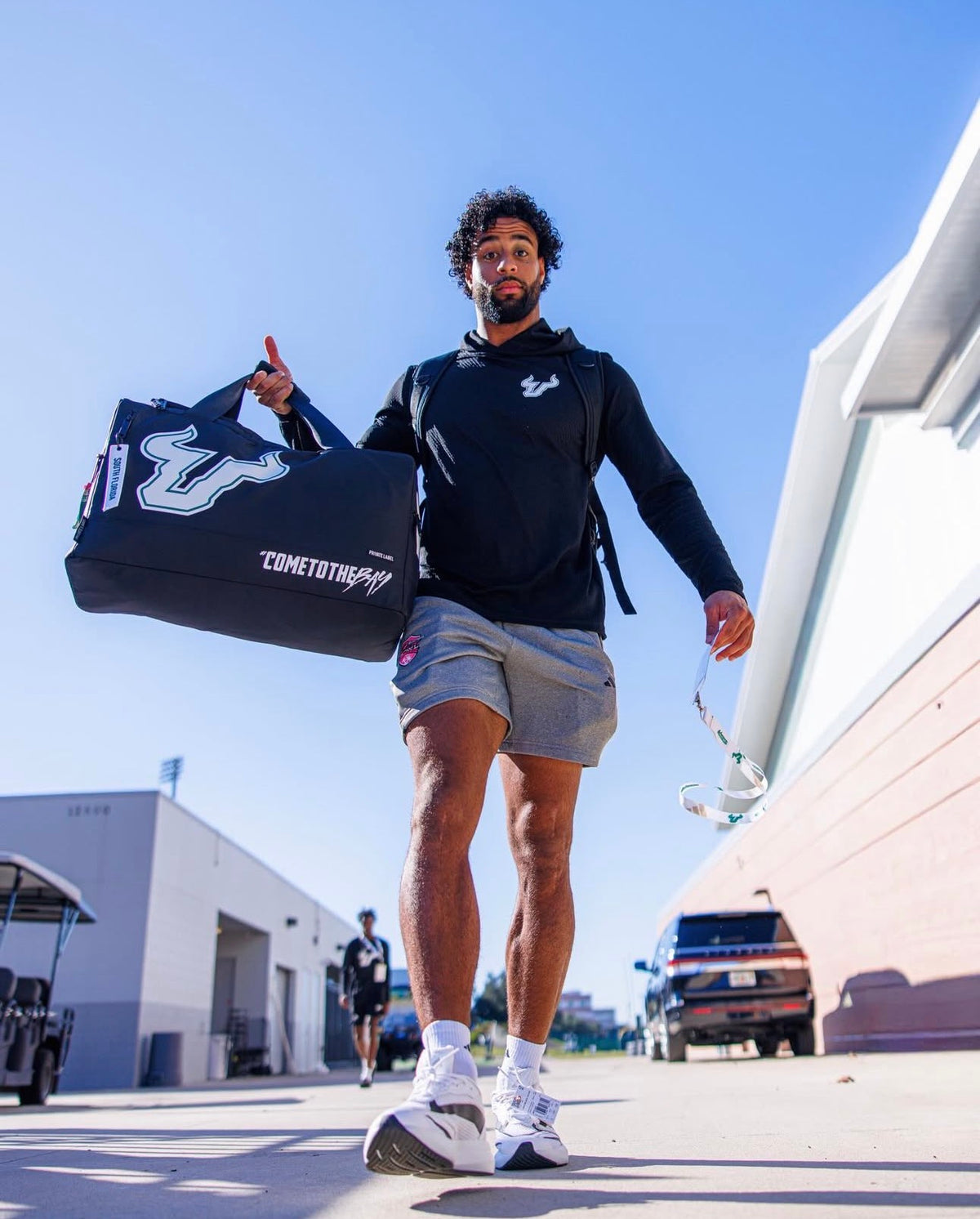 Person holding a sports bag with a clear blue sky background