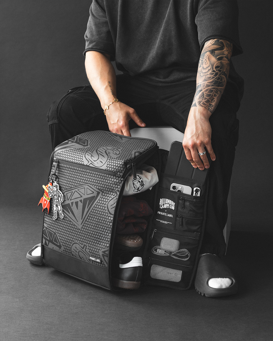 model sitting next to an open backpack containing assorted items such as shoes & clothes + accessories
