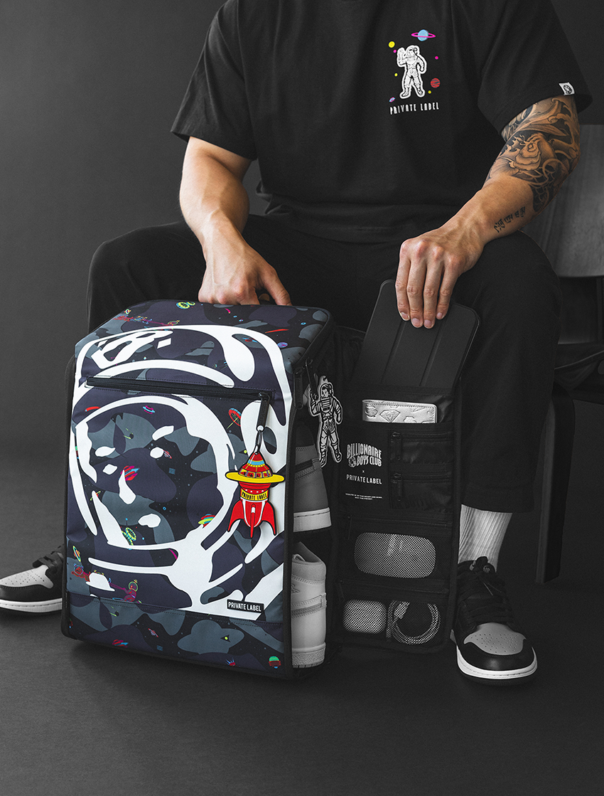 space camo themed backpack with the bbc helmet logo on the outside with a model pulling out a tablet from the backpack pocket
