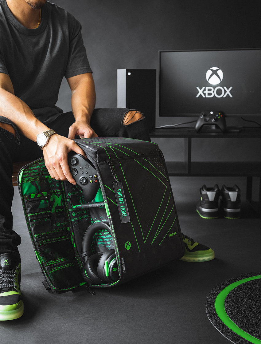 person taking out a console controller from a black backpack with green xbox stripes